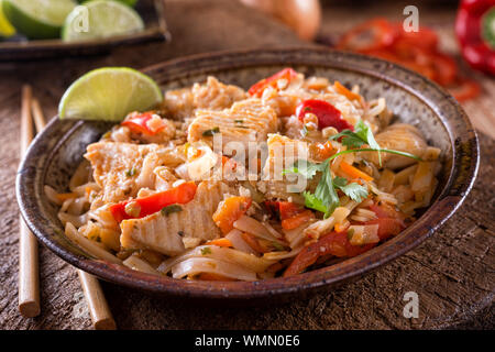 Un bol de poulet délicieux pad thaï avec des nouilles de riz, poivron rouge, carotte, arachide, ciliantro et lime. Banque D'Images