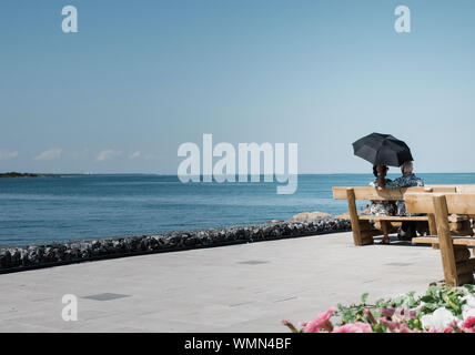 Romantique retraite couple sitting on bench avec parapluie à la recherche en mer Banque D'Images