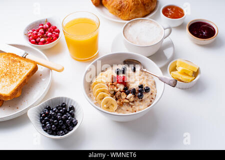 Le petit-déjeuner avec du gruau avec des baies et des noix, des croissants, des toasts avec du beurre et de la confiture, du café et du jus d'orange Banque D'Images