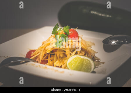 Thai salade de papaye verte avec la papaye verte, tomates cerises, noix de cajou et servi sur une assiette de porcelaine blanche Banque D'Images