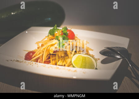 Thai salade de papaye verte avec la papaye verte, tomates cerises, noix de cajou et servi sur une assiette de porcelaine blanche Banque D'Images