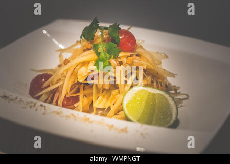 Thai salade de papaye verte avec la papaye verte, tomates cerises, noix de cajou et servi sur une assiette de porcelaine blanche Banque D'Images