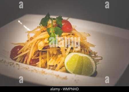 Thai salade de papaye verte avec la papaye verte, tomates cerises, noix de cajou et servi sur une assiette de porcelaine blanche Banque D'Images