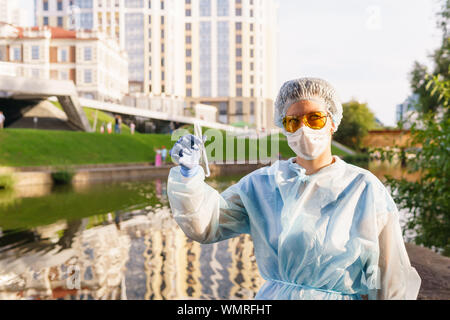 Femme dans un masque de protection écologiste regardant la caméra tenant un tube à essai avec de l'eau d'une rivière de la ville Banque D'Images