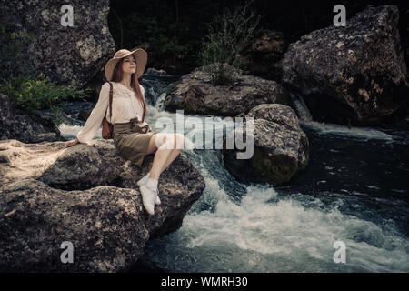Woman traveler avec sac à dos et hat walking in amazing montagnes et forêt près de rivière avec de l'eau d'un bleu profond Banque D'Images