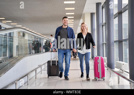 Droit de marcher heureux homme et femme marchant le long de la passerelle avec des valises à l'aéroport au jour Banque D'Images