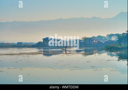 Le villageois est debout sur le bord de la pêche de kayak sur l'étang de montagne brumeuse Tharzi avec silhouette sur arrière-plan, Nyaungshwe, Myanmar. Banque D'Images