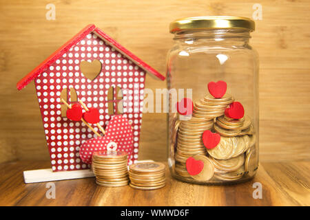 Bocal en verre avec des pièces d'or et rouge petit coeur et de la chambre. Économiser de l'argent pour acheter une maison ou pour se marier. Banque D'Images