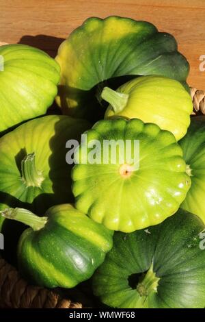 Green Patty pan scallop courges bordée de différentes tailles dans un panier au soleil avec du parquet en chêne dans l'arrière-plan Banque D'Images