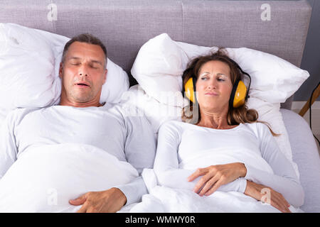 Femme mature couvrant ses oreilles avec casque tandis que l'Homme le ronflement au lit Banque D'Images