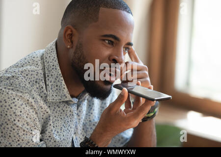 Close up thoughtful african american guy à l'aide d'assistant virtuel. Banque D'Images