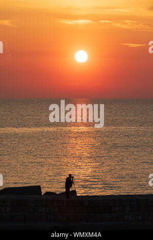 Italie, Pouilles, province de Lecce, Gallipoli. Un photographe qui se profile dans le coucher du soleil sur la mer Ionienne. Banque D'Images