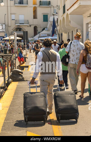 Île de Capri, ITALIE - AOÛT 2019 : personne tirant valises sur le chemin de ronde autour du port dans le port sur l'île de Capri Banque D'Images