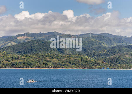 Caticlan, Malay, Philippines - Le 4 mars 2019 : gamme de montagne verte avec des moulins dispersés sous ciel bleu avec des nuages épais gris. Blue Sea avec sm Banque D'Images