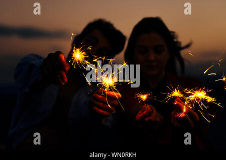 Outdoor portrait of young beautiful happy smiling couple posing on mountain. Jeune couple avec feu de Bengale dans le noir Banque D'Images