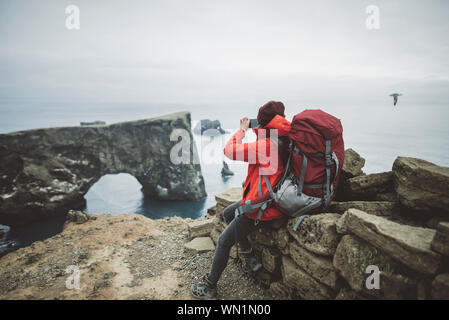 Female hiker photographing arche naturelle dans la région de Vik, Islande Banque D'Images