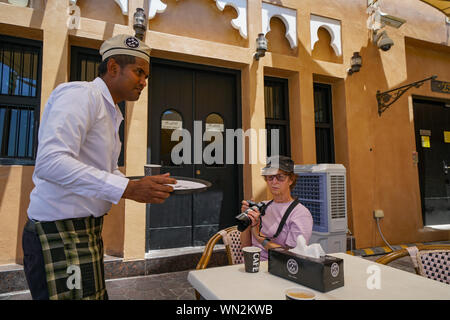 DOHA, QATAR - 10 juillet 2019 ; Middle Eastern waiter serving caucasian woman with camera café traditionnel verre connu un karak dans Villa culturel Katara Banque D'Images