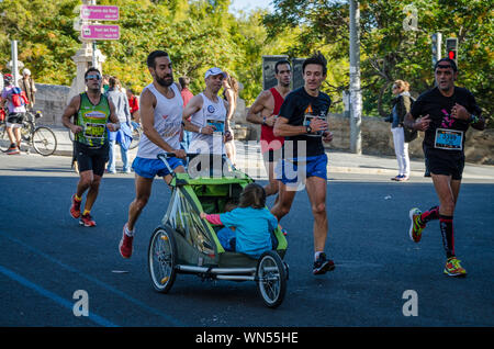 Homme qui va pousser son fils dans la voiture de marathon de Valence en Espagne le 16 novembre 2014 Banque D'Images