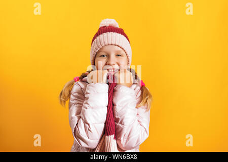 Portrait of a cute little girl dans une veste, écharpe et chapeau sur un fond jaune. Concept d'automne et d'hiver. Banque D'Images