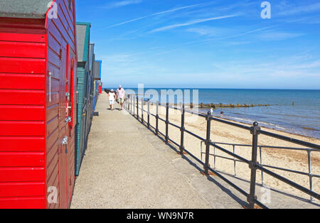 Un couple sur la promenade par des cabines de plage à la station balnéaire de Mundesley, Norfolk, Angleterre, Royaume-Uni, Europe. Banque D'Images