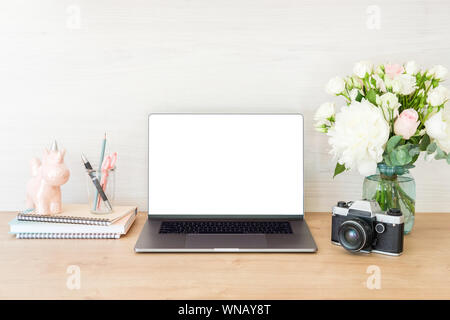 Ordinateur portable avec de l'espace écran blanc et de fournitures de bureau à bureau de travail. Table bureau féminin avec ordinateur portable, appareil photo, film, fleurs unic Banque D'Images