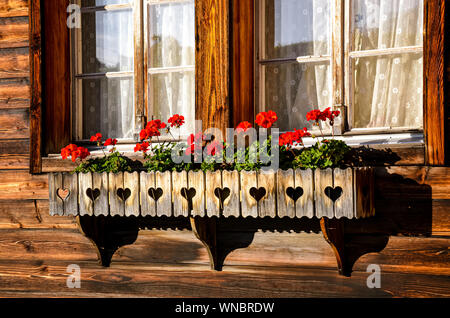 Fleurs rouge typique dans les fenêtres de style alpin chalets en bois. Cabane en bois de Bavière. Décoration florale. Tradition, style. La Bavière, l'Autriche, Alpes Suisses. Banque D'Images