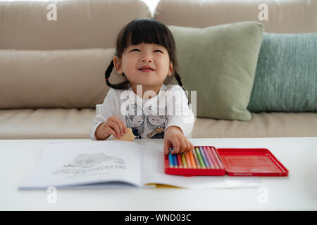 Happy Asian girl avec un grand sourire tout en mangeant lorsqu'elle tranche dessin dans salle de séjour chez elle. Banque D'Images