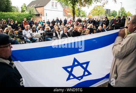 06 septembre 2019, Basse-Saxe, Wilhelmshaven : Les participants se tiennent debout derrière un drapeau israélien lors de la commémoration à la cérémonie de commémoration du sort des réfugiés juifs dans le nord de l'Allemagne en 1947. Les survivants de l'Holocauste et de la famille visiter les anciens camps à Emden et Wilhelmshaven. L'Odyssée des réfugiés juifs en Palestine avec le navire 'exode' avait fait les manchettes dans le monde entier en 1947. Les réfugiés ont dû faire marche arrière et attendre des mois dans des casernes pour l'Allemagne du Nord une nouvelle autorisation de sortie. Photo : afp/Assanimoghaddam Mohssen Banque D'Images