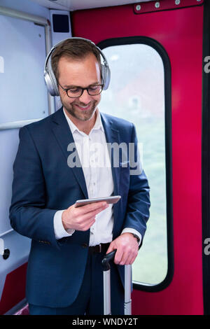 Businessman Standing On Train Film Streaming à partir d'un téléphone portable sur un casque sans fil Banque D'Images