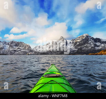 Petit kayak dans le fjord de la baie verte dans les Lofoten, entouré de montagnes de neige et ciel bleu. La Norvège Banque D'Images