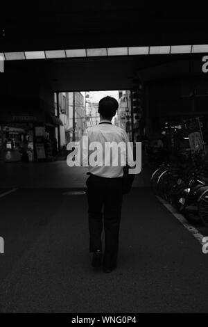 MATSUYAMA, JAPON - 21 août 2019 : un gris vertical vue d'un homme portant des vêtements formels marche sur une route près de bicyclettes garées Banque D'Images