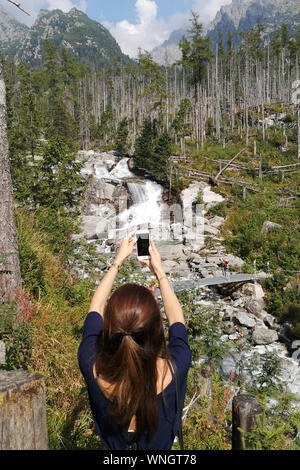 Une femme s'arrête pour photographier les cascades du ruisseau Cold, Stary Smokovec Cascades, dans les Hautes Tatras, en Slovaquie, le 31 août 2019. Banque D'Images