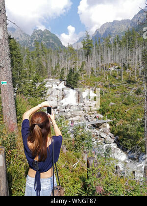 Une femme s'arrête pour photographier les cascades du ruisseau Cold, Stary Smokovec Cascades, dans les Hautes Tatras, en Slovaquie, le 31 août 2019. Banque D'Images