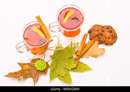 Automne verre concept. Vin chaud ou chocolat chaud dans wineglasses avec des bâtons de cannelle. Verres avec du vin ou boisson chaude près de feuilles d'automne et les cookies sur fond blanc, Close up. Banque D'Images