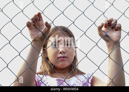 Sad girl derrière metal wire mesh fence. Enfant solitaire et abandonnée à l'extérieur. Déprimé preteen aux yeux clos tenant la cage d'acier chaîne. Loneline Banque D'Images