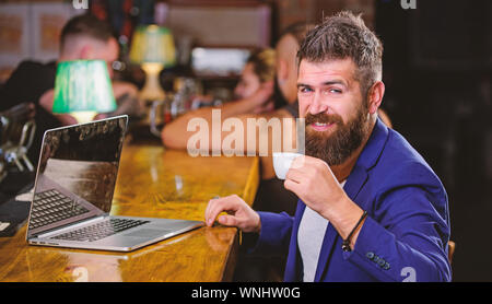 Offres de prestation. Le travail du gestionnaire en ligne alors que prendre un café. Hipster freelancer travailler en ligne blog ordinateur portable. Surfer sur internet. Emploi en ligne. Homme barbu homme siéger pub avec ordinateur portable et tasse de café. Banque D'Images