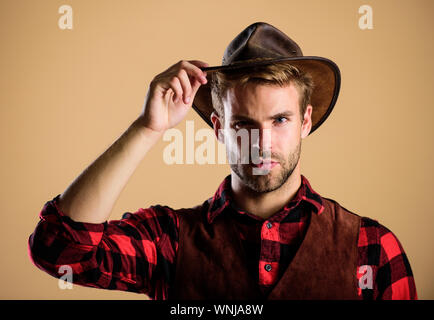 Port de Cowboy hat. American Cowboy. Norme de beauté. Exemple d'une véritable masculinité. La vie dans l'Ouest. Homme cowboy non rasé beige background. Guy non rasé en chapeau de cowboy. Beau macho barbu. Banque D'Images