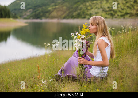 Woman smelling flowers tout en passant du temps dans la magnifique nature. Banque D'Images