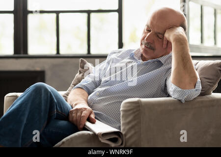 Fatigué senior hispanic man with newspaper dormir sur la table, en prenant de l'après-midi à la salle de séjour Banque D'Images