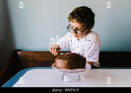 Le Tween boy frosting son gâteau d'anniversaire avec glaçage au chocolat.o Banque D'Images