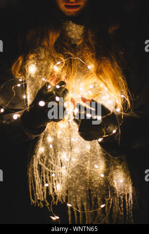 Jeune femme tenant les lumières de Noël à l'extérieur dans le noir Banque D'Images