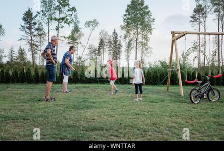 Les grands-parents de jouer avec leurs petits-enfants en sautant et en dehors du vélo Banque D'Images