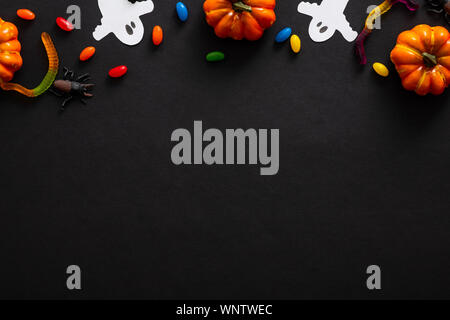 La composition de l'Halloween avec des citrouilles, fantômes, des bonbons sur fond noir. Halloween party invitation card immersive. Mise à plat, vue du dessus, copiez l'espace. Banque D'Images