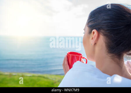 Girl enveloppé dans une couverture sur le balcon le matin boit du café ou thé. Banque D'Images