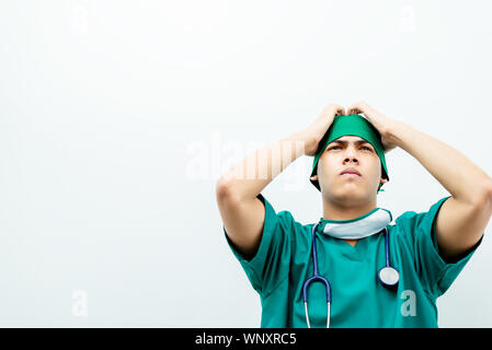 Jeune médecin asiatique sérieusement les mains des hommes sur le front du patient pour le traitement déçu .Médecin chirurgie en uniforme vert avec stéthoscope isolé sur Banque D'Images