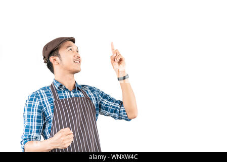 Le jeune homme asiatique qui est portant un tablier, sourire avec confiance et pointe vers quelque chose au-dessus de lui isolé sur fond blanc. Portrait man avec copie sp Banque D'Images