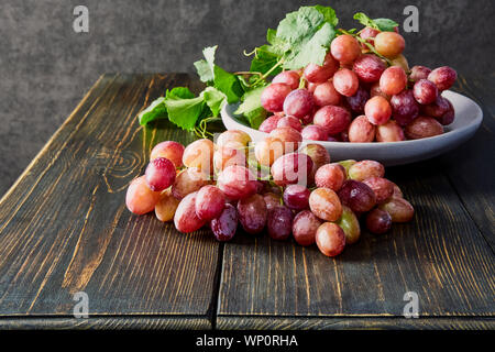 Les raisins frais. Bouquets de différentes variétés dans une assiette sur une vieille table en bois et un arrière-plan sombre. soft focus Banque D'Images