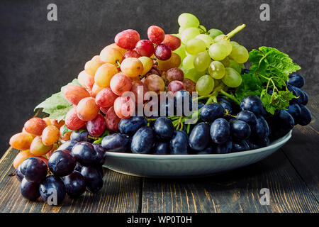 Les raisins frais. Bouquets de différentes variétés dans une assiette sur une vieille table en bois et un arrière-plan sombre. soft focus Banque D'Images