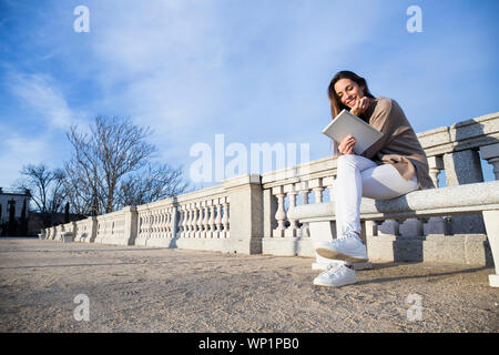 Laughing woman using her tablet tout en étant assis sur un banc Banque D'Images