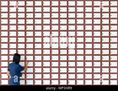 Une jeune femme ouvre boîte aux lettres sur mur plein de boîtes aux lettres. Femme à l'aide de boîtes de dépôt sur le mur. Banque D'Images